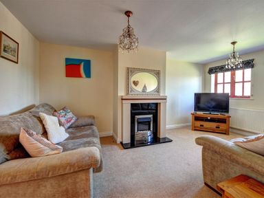 A living room with two sofas a fireplace a television and two chandeliers at 28 Barnes Meadow in Uplyme