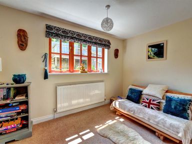 A small living room with a futon sofa with cushions a window with patterned blinds and a bookshelf at 28 Barnes Meadow in Uplyme