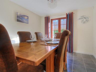 A dining room with a wooden table set with plates and wine glasses and brown chairs at 28 Barnes Meadow in Uplyme