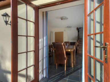Dining area with wooden table and chairs viewed through open glass doors at 28 Barnes Meadow in Uplyme