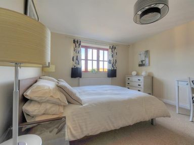 A bedroom with a double bed a bedside lamp a window with curtains a chest of drawers and a desk at 28 Barnes Meadow in Uplyme