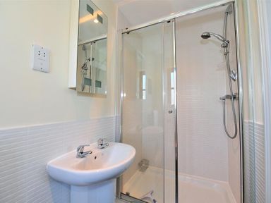A bathroom with a double faucet sink and a glass-enclosed shower with a showerhead at 28 Barnes Meadow in Uplyme