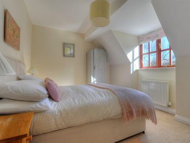 A bedroom with a bed with pillows and a blanket a window with wooden frames and a radiator at 28 Barnes Meadow in Uplyme