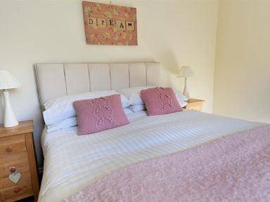A bedroom with a double bed two pink cushions bedside tables with lamps and a dream sign above the bed at 28 Barnes Meadow in Uplyme