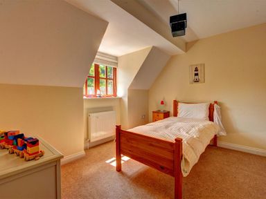 A bedroom with a wooden bed a bedside table and a toy train on a dresser at 28 Barnes Meadow in Uplyme