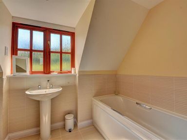 A bathroom with a pedestal sink a bathtub a window with frosted panes and a small trash can at 28 Barnes Meadow in Uplyme