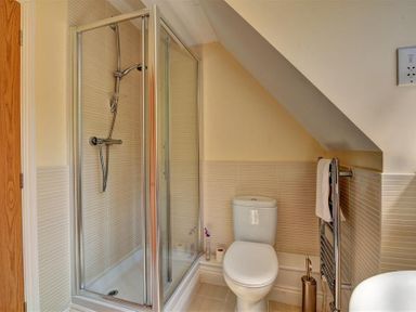 A bathroom with a shower enclosure a toilet a towel rack and a slanted ceiling at 28 Barnes Meadow in Uplyme