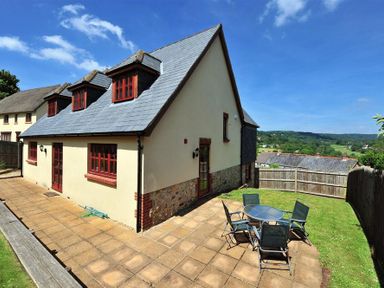 A house with a patio and outdoor table with chairs in a backyard at 28 Barnes Meadow in Uplyme