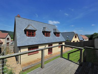 View of a house with a tiled roof and red-framed windows from a wooden deck with railing at 28 Barnes Meadow in Uplyme