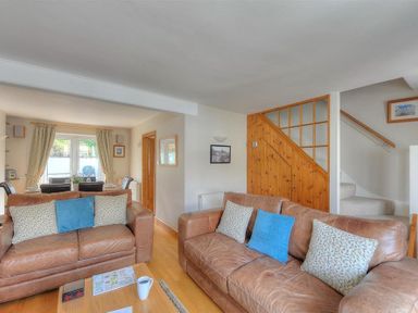 A living room with leather sofas and cushions next to a wooden staircase at Ivy Cottage in Beer