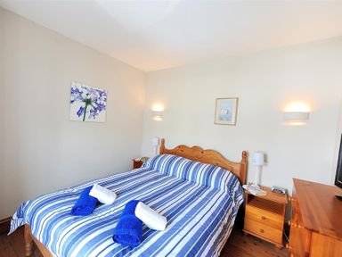 A bedroom with a double bed with blue and white striped bedding two bedside tables with lamps and paintings on the walls at Ivy Cottage in Beer