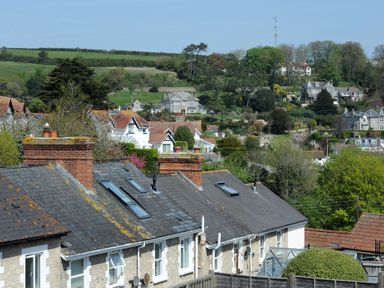 Roofs and chimneys of stone houses with a hillside and more houses in the background at Ivy Cottage in Beer