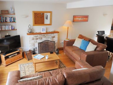 A living room with brown leather sofas a wooden coffee table a television and a stone fireplace at Ivy Cottage in Beer
