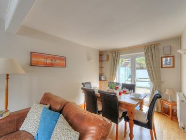 A dining area with a wooden table set for four and a brown leather sofa with cushions in a room with curtains at Ivy Cottage in Beer