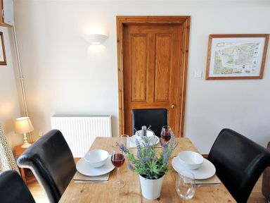 A dining table set with plates bowls glasses and a plant in a room with a wooden door and wall lamp at Ivy Cottage in Beer