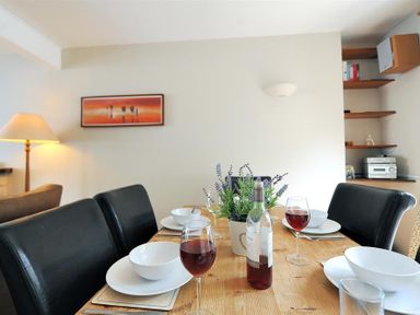 A dining table set with bowls plates glasses and wine in a room with shelves and a lamp at Ivy Cottage in Beer