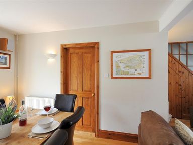 A dining area with a wooden table set with dishes and wine glasses near a wooden door and a staircase at Ivy Cottage in Beer
