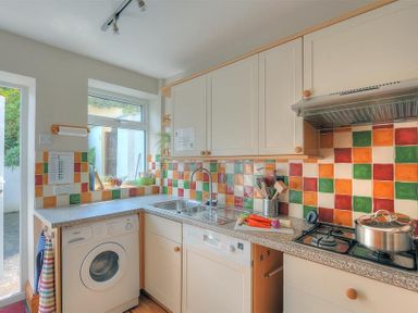 A kitchen with colorful tiled backsplash a washing machine a sink carrots on the countertop and a stove with a pot at Ivy Cottage in Beer