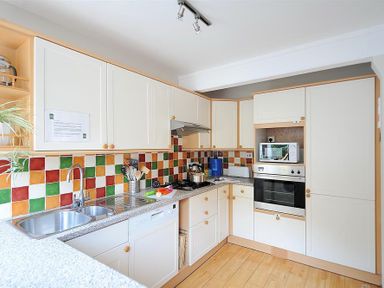 A kitchen with white cabinets a double sink a built in oven a microwave and a tiled backsplash at Ivy Cottage in Beer