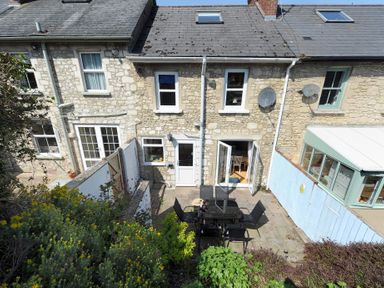A stone house with a small patio area with a table and chairs and some plants at Ivy Cottage in Beer