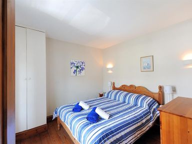 A bedroom with a wooden bed with blue and white striped bedding and towels on the bed at Ivy Cottage in Beer