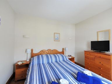 A bedroom with a double bed with striped bedding two wooden bedside tables with lamps wooden dresser with a television and a mirror at Ivy Cottage in Beer