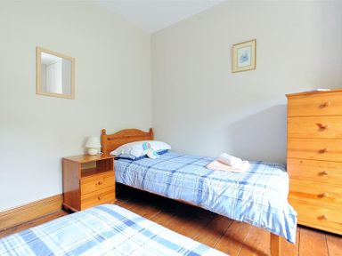 A bedroom with two single beds a wooden nightstand with a lamp a wooden chest of drawers a framed picture and a wall mirror at Ivy Cottage in Beer