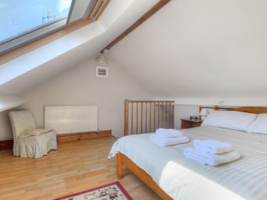 A bedroom with a wooden bed and white linens with towels on top a floral chair and a skylight window at Ivy Cottage in Beer