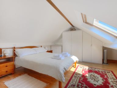 A bedroom with a double bed white linens wooden nightstands rugs and a skylight window at Ivy Cottage in Beer