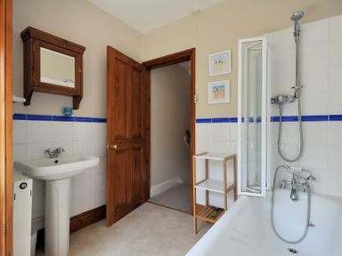 A bathroom with a bathtub shower combo a pedestal sink a wooden medicine cabinet and a wooden door at Ivy Cottage in Beer