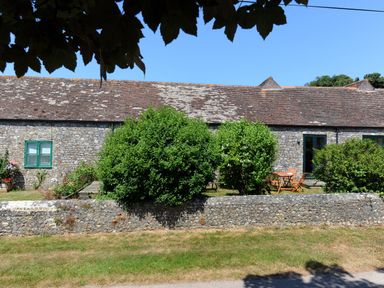 A stone building with green windows and a brown tiled roof behind green bushes and a low stone wall at 3 Home Farm South in Rousdon