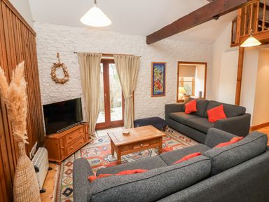 A living room with two gray sofas with red pillows a wooden coffee table a television on a wooden stand and French doors at 3 Home Farm South in Rousdon