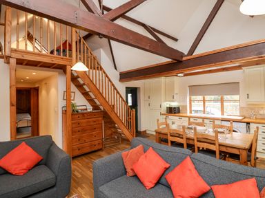 A living room with gray sofas and red cushions a wooden dining table and chairs wooden staircase and exposed beams at 3 Home Farm South in Rousdon