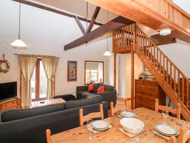 An open living and dining area with wooden furniture stairs and sofas at 3 Home Farm South in Rousdon