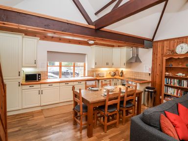 A kitchen with wooden dining table and chairs a grey sofa with red cushions and wooden shelves at 3 Home Farm South in Rousdon