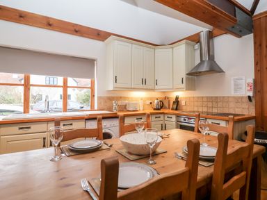 A kitchen with wooden dining table set with plates and glasses and cream cabinets at 3 Home Farm South in Rousdon