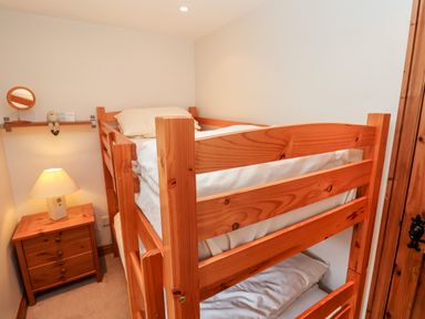 A small bedroom with wooden bunk beds a wooden nightstand with a lamp and a small wall shelf with a mirror at 3 Home Farm South in Rousdon