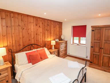 A bedroom with a bed and bedside tables with lamps wooden cupboards and a window with a red blind at 3 Home Farm South in Rousdon