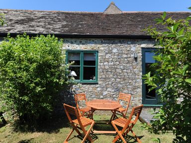 A stone wall house with green windows and a wooden table and chairs outside at 3 Home Farm South in Rousdon