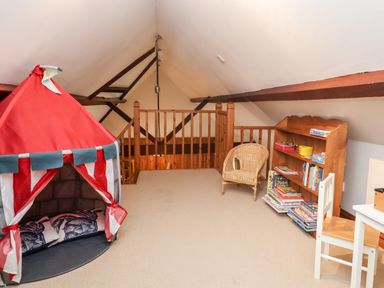 An attic playroom with a red tent a wicker chair a wooden bookshelf and a small table with a chair at 3 Home Farm South in Rousdon