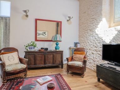 A living room with armchairs and a television at The Stone Barn in Bridport