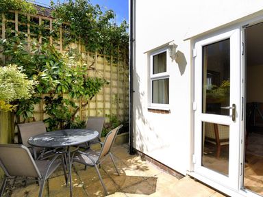 A small outdoor patio with a round table and four chairs next to a white building with a door and window at Vine Cottage in Charmouth