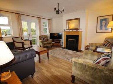 A living room with armchairs a sofa a coffee table a fireplace a television and double doors at Vine Cottage in Charmouth