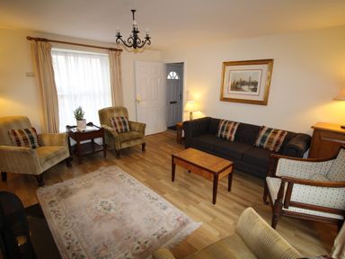 A living room with armchairs a sofa a wooden coffee table a rug a side table with a plant and a framed picture on the wall at Vine Cottage in Charmouth