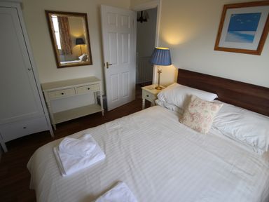 A bedroom with a double bed with white linens a bedside table with a lamp a mirror above a console table and a framed picture on the wall at Vine Cottage in Charmouth