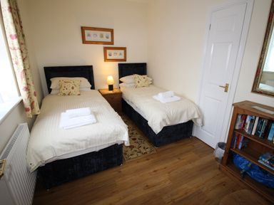 A bedroom with twin beds a bedside table a lamp a bookshelf and a door at Vine Cottage in Charmouth