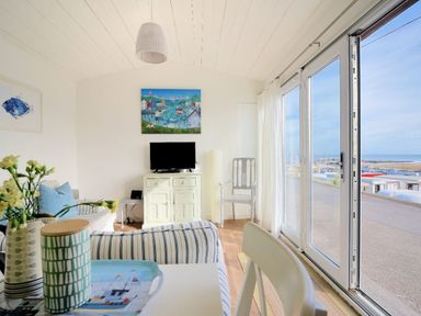 A living area with striped sofas a television on a cabinet and large sliding glass doors overlooking a marina at The Beach Hut in Lyme Regis