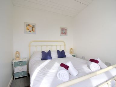 A bedroom with a bed with white bedding and blue pillows and nightstands with lamps at The Beach Hut in Lyme Regis