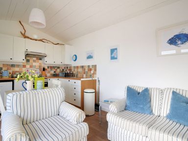A kitchen and living area with striped sofa and armchair and tiled backsplash at The Beach Hut in Lyme Regis