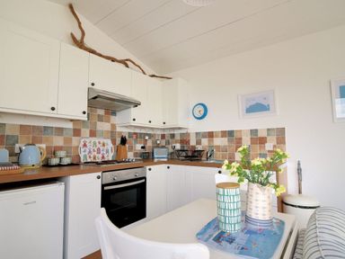 A kitchen with white cabinets multicolored tile backsplash and small dining table at The Beach Hut in Lyme Regis